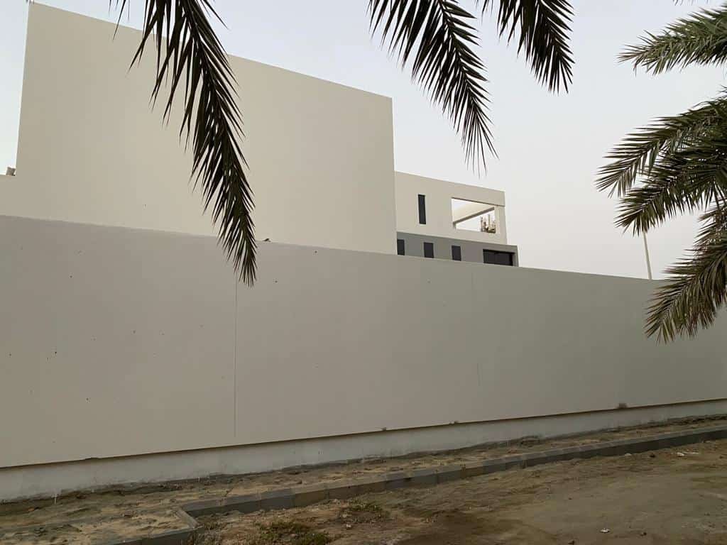 INJ Architects مسبح مبلط باللون الأزرق قيد الإنشاء بجوار واجهة زجاجية سوداء طويلة وأبراج سقالات معدنية