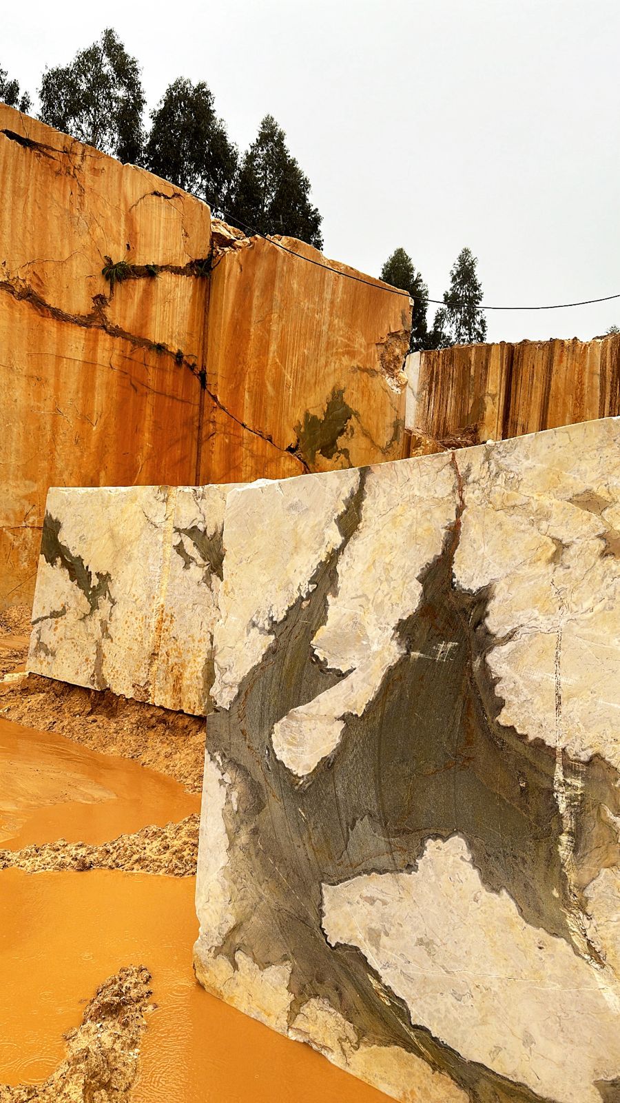 Large quarried marble blocks with grey veining resting in an open-pit stone quarry with orange rock walls