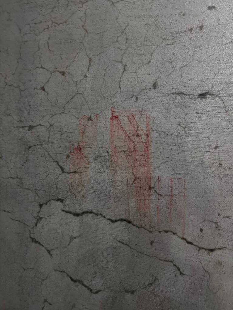 Macro view of a cured cement plaster surface displaying hairline shrinkage cracks and red site engineering marking sketches.