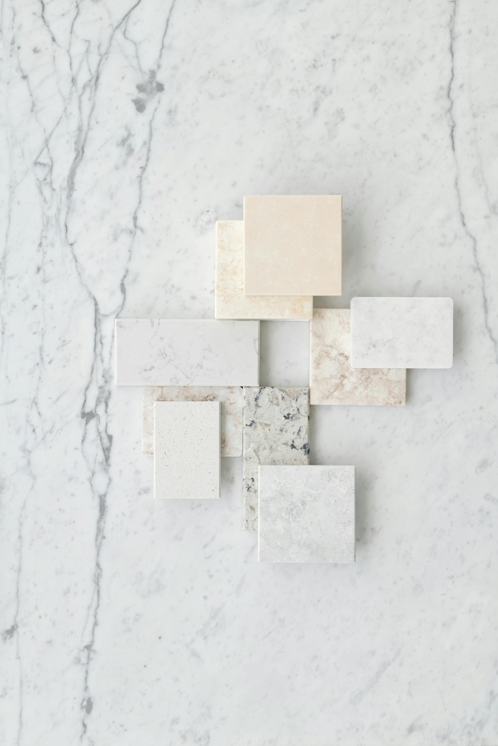 Aesthetic flat lay of various marble tiles arranged on a textured marble surface.