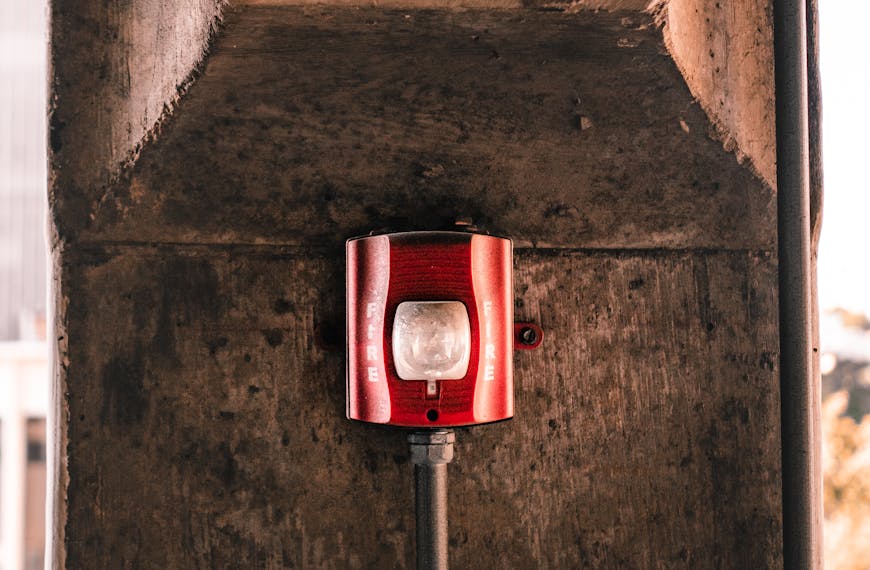 Red fire alarm on a concrete wall in urban environment, symbolizing safety and security.