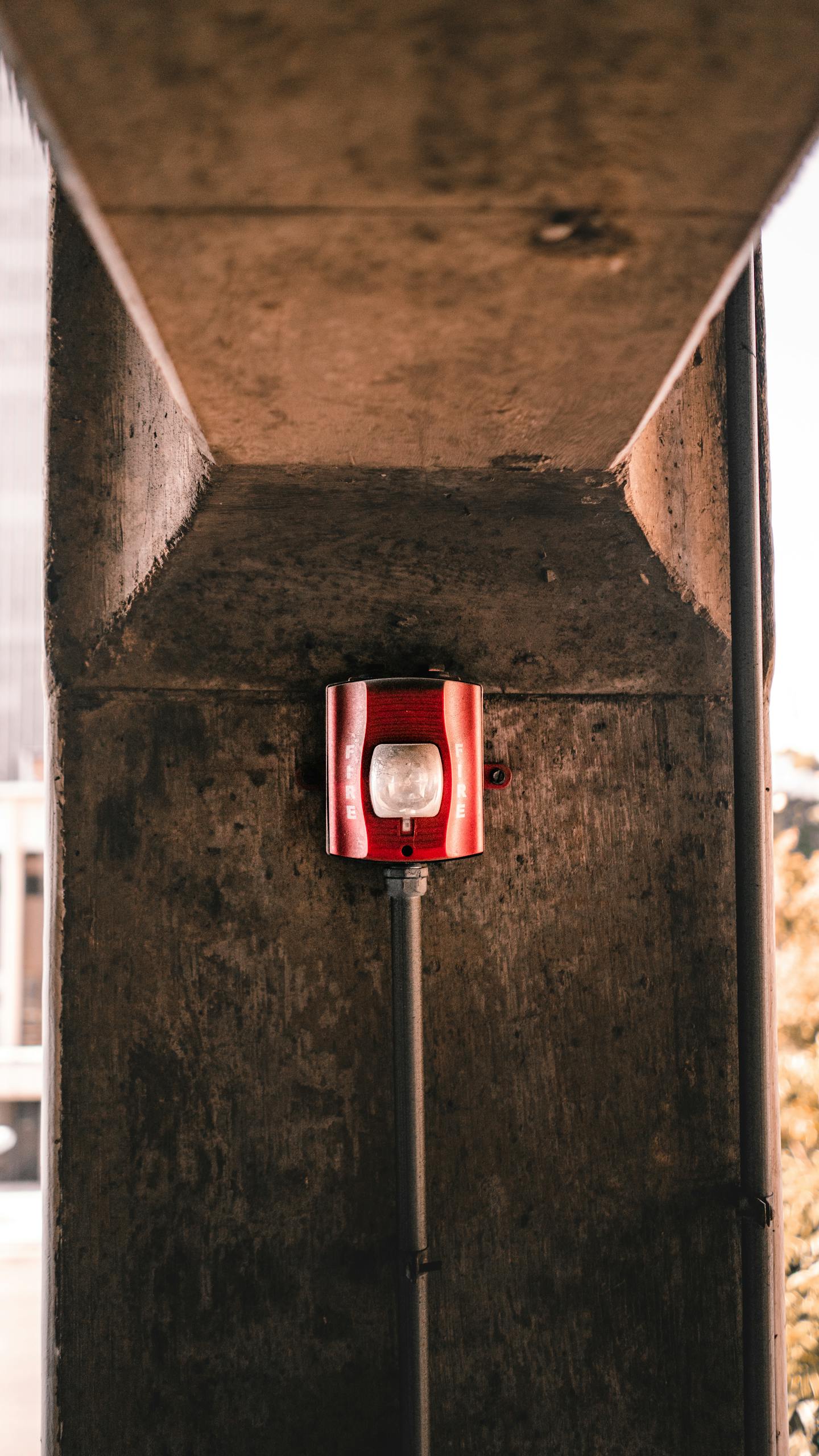 Red fire alarm on a concrete wall in urban environment, symbolizing safety and security.