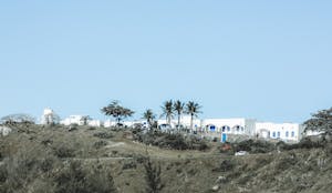 Scenic view of Mediterranean-style villas on a hill with clear blue skies and palm trees.