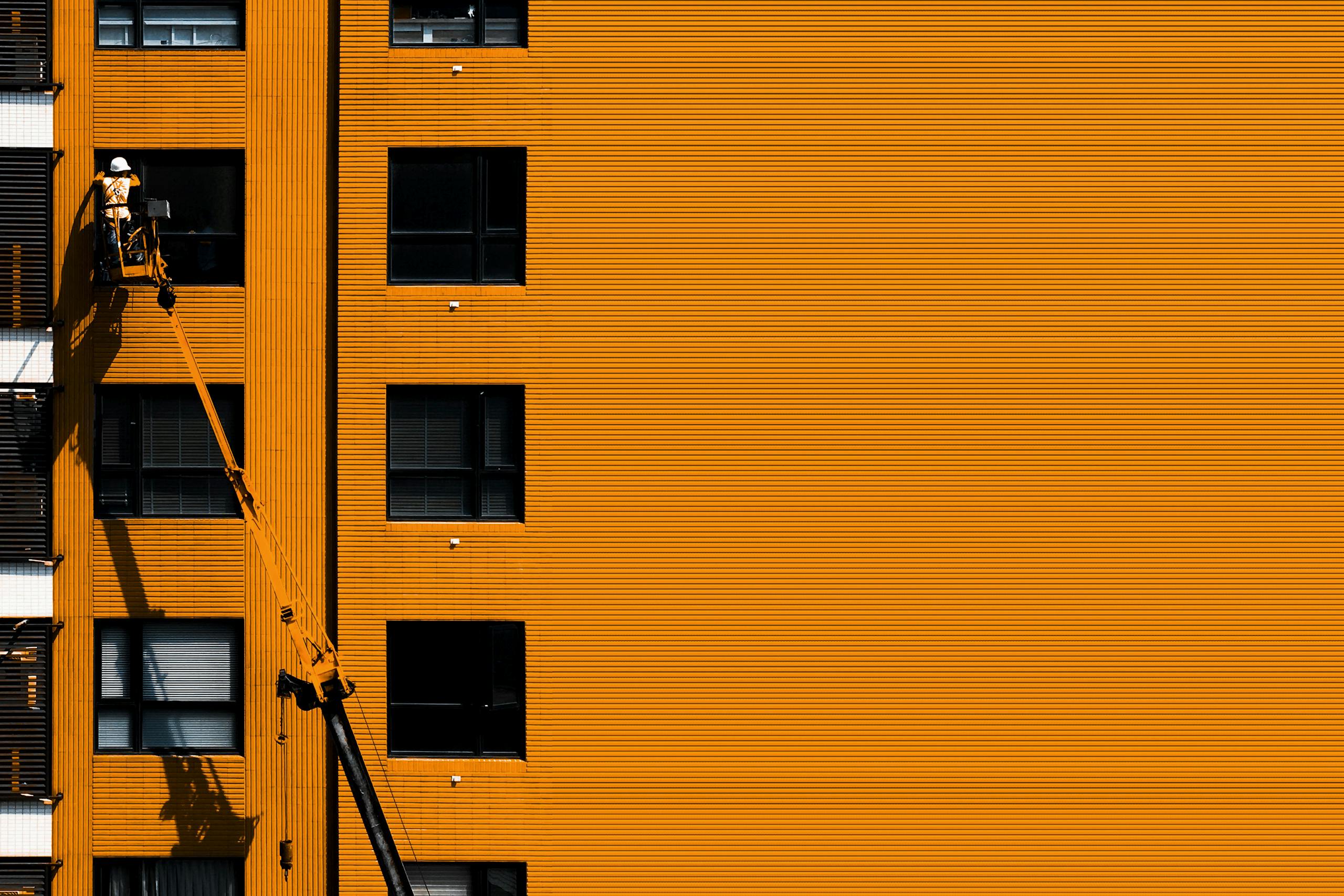 A construction worker using a cherry picker working on an orange building facade.