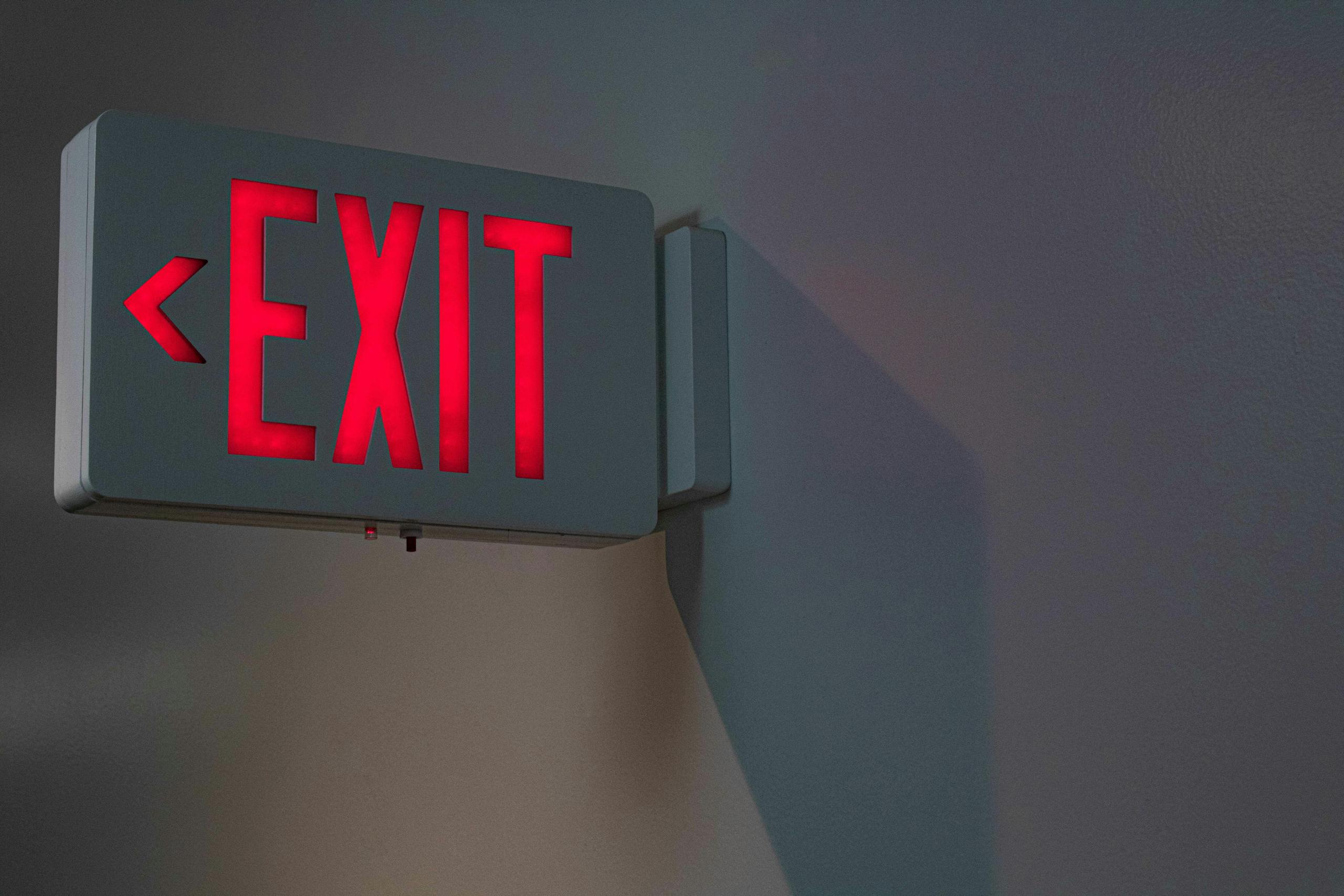 Close-up of a lit red exit sign on a gray wall, ideal for emergency and safety themes.
