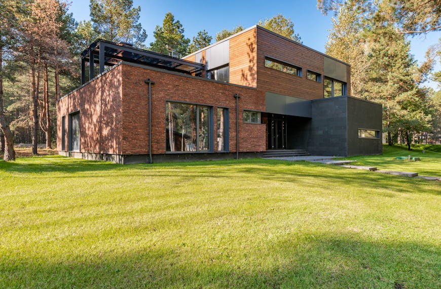 Contemporary brick house featuring large glass windows surrounded by lush green lawn.