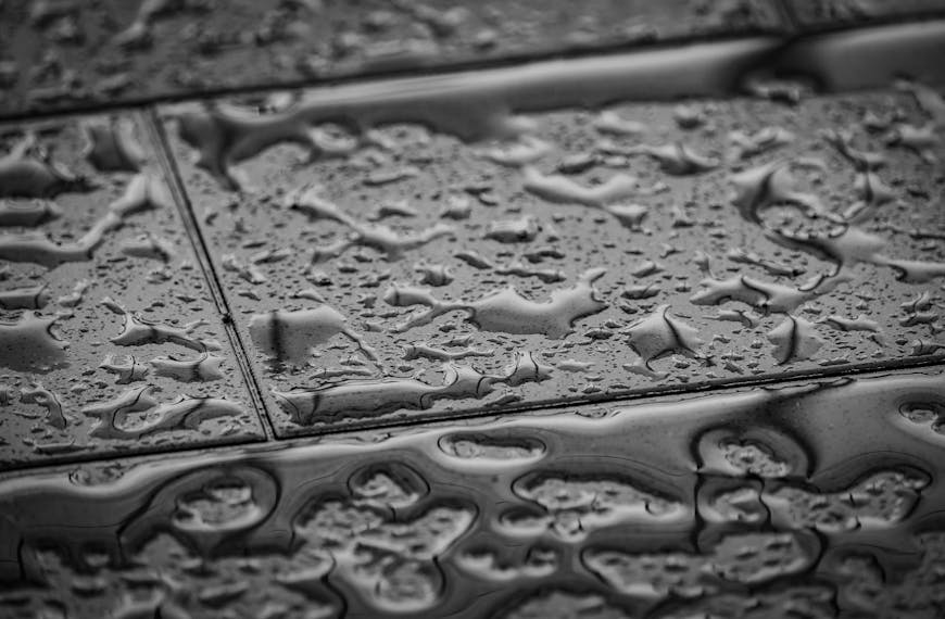 Grayscale close-up image of wet tiles with water droplets creating an abstract texture.