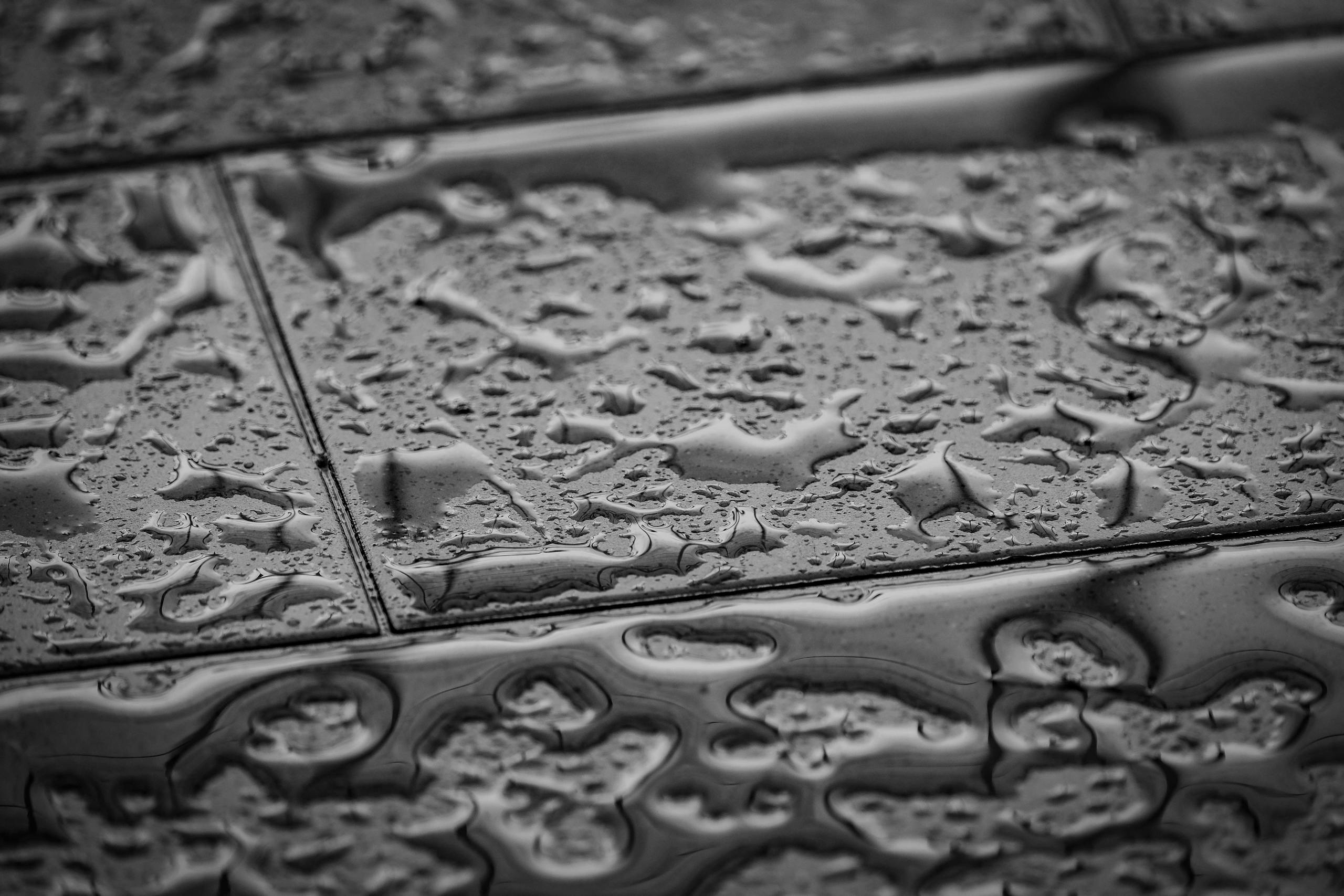 Grayscale close-up image of wet tiles with water droplets creating an abstract texture.