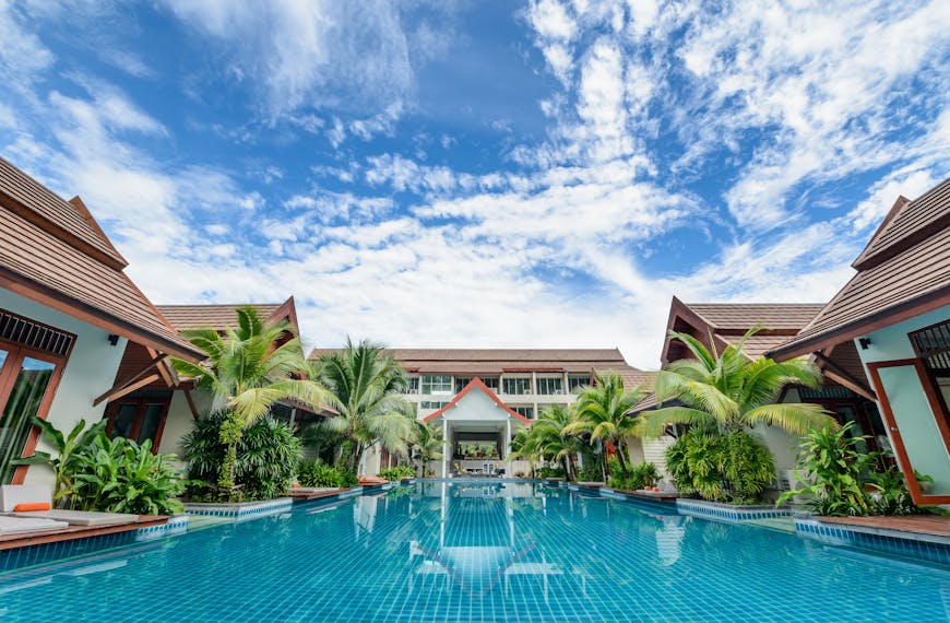 Spacious swimming pool surrounded by tropical villas under a bright blue sky, perfect for relaxation.