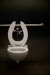 A modern toilet with a safety rail in a public restroom, featuring a minimal design.