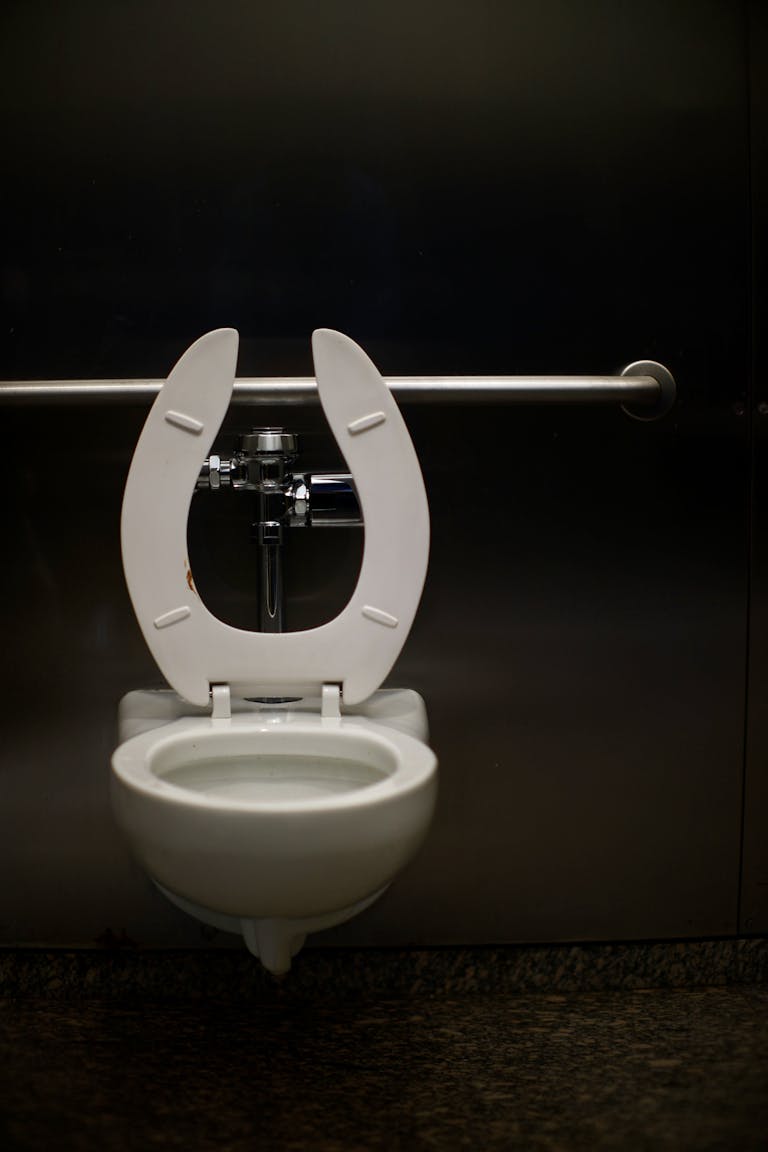 A modern toilet with a safety rail in a public restroom, featuring a minimal design.