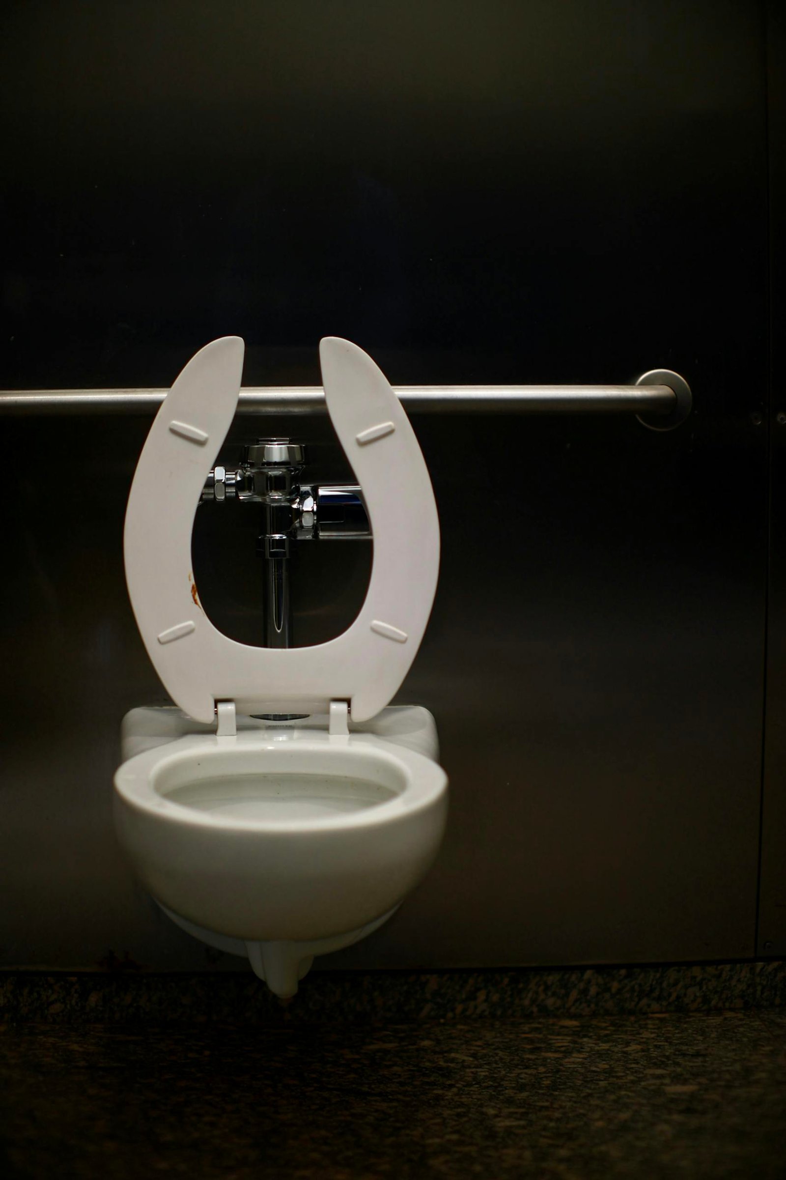 A modern toilet with a safety rail in a public restroom, featuring a minimal design.