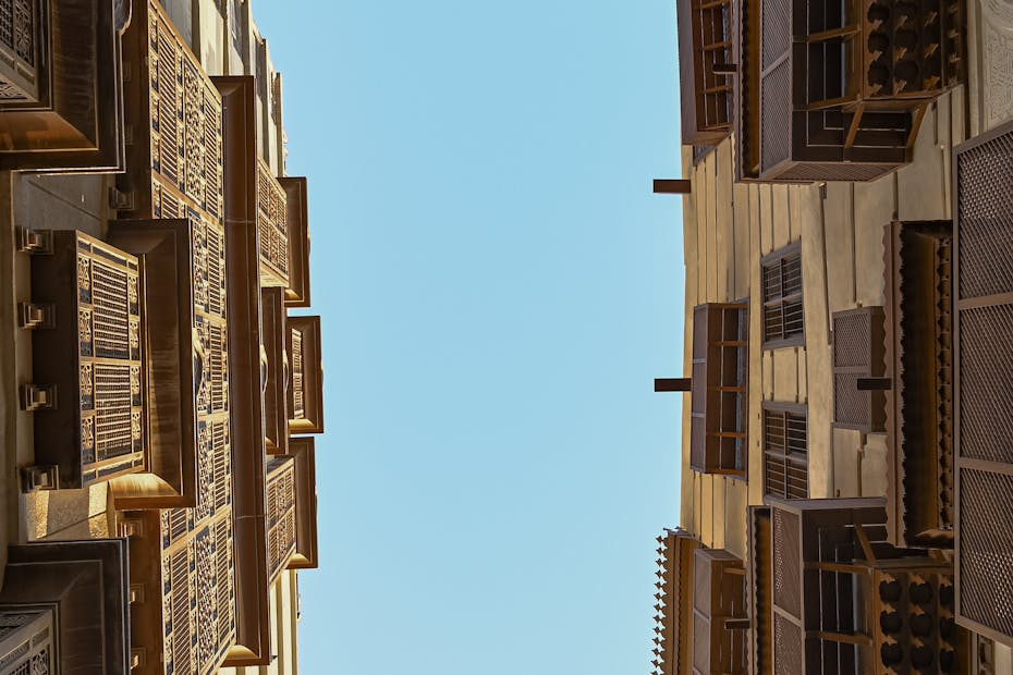 Upward view of buildings with intricate mashrabiya designs against a clear blue sky.