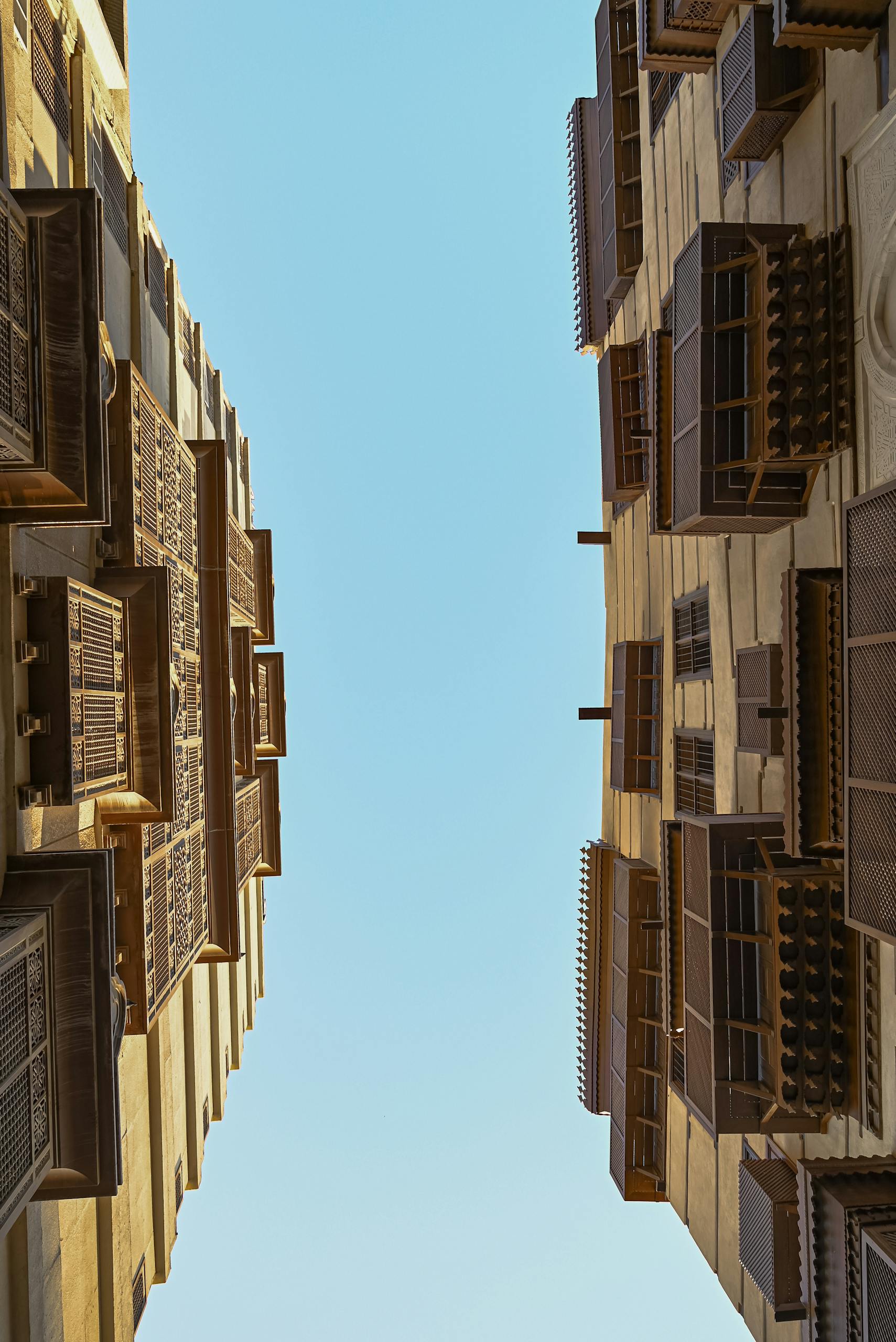 Upward view of buildings with intricate mashrabiya designs against a clear blue sky.