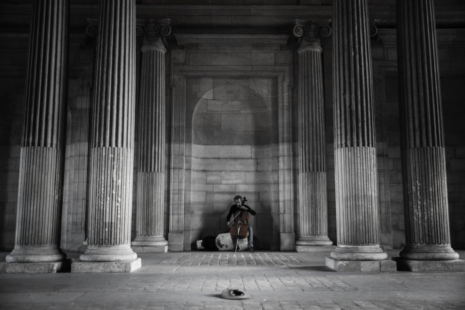A street musician plays the cello amidst grand columns in Paris, creating a serene atmosphere.