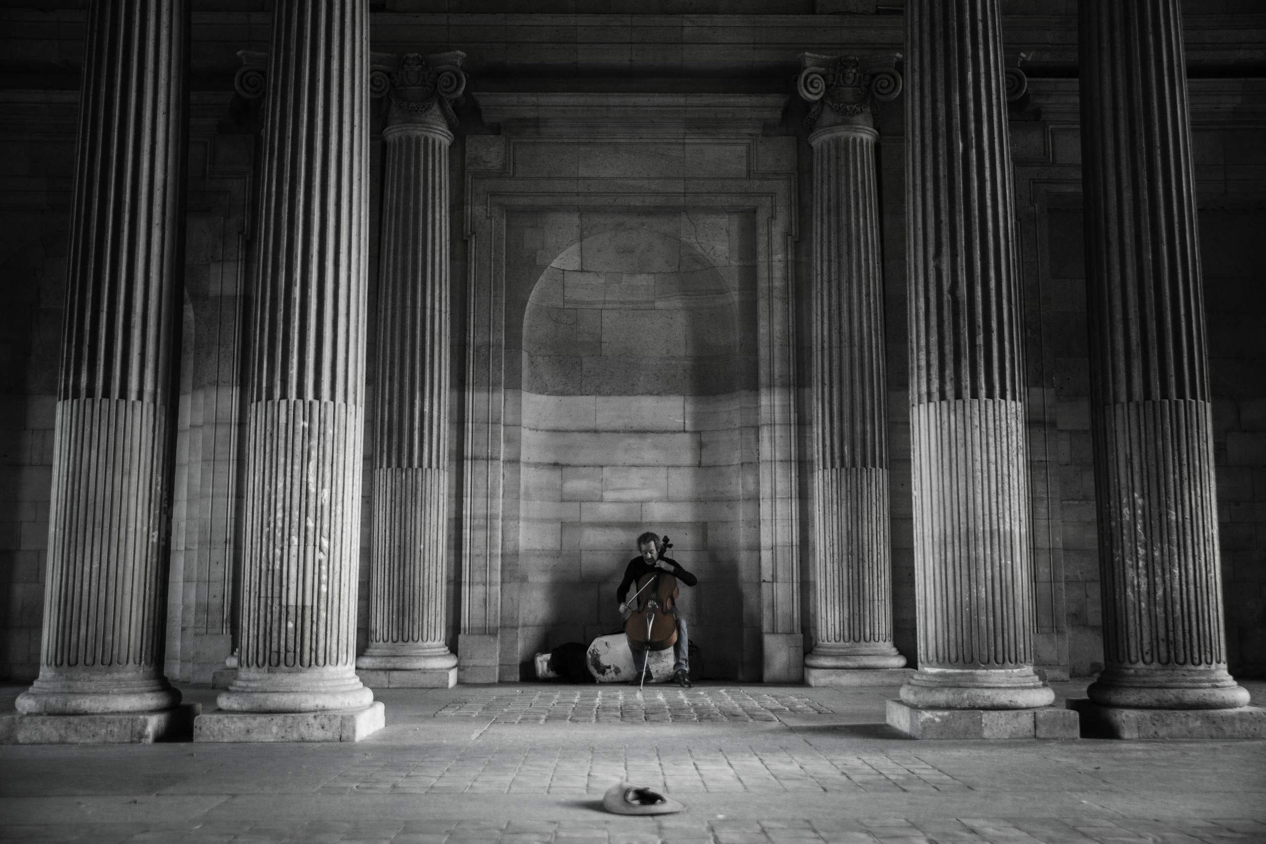 A street musician plays the cello amidst grand columns in Paris, creating a serene atmosphere.