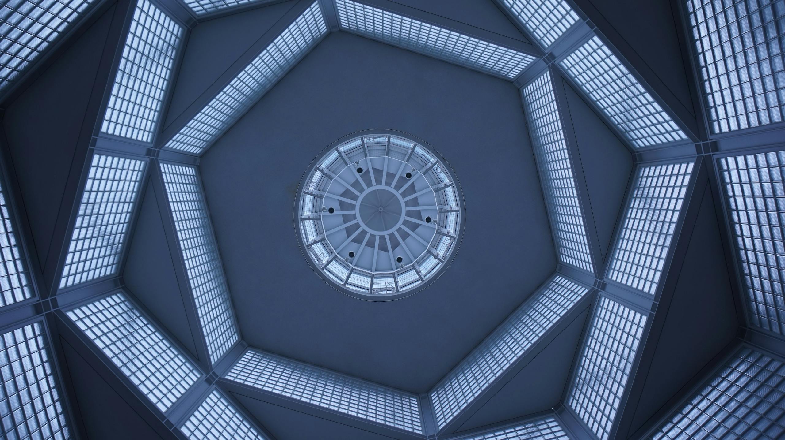 Futuristic glass ceiling architecture with geometric patterns viewed from below, emphasizing symmetry and perspective.