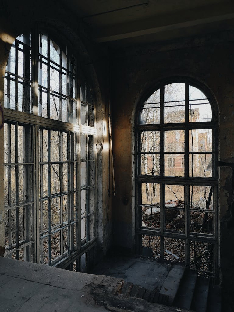 Interior of an abandoned building with large broken windows and sunlight streaming through.