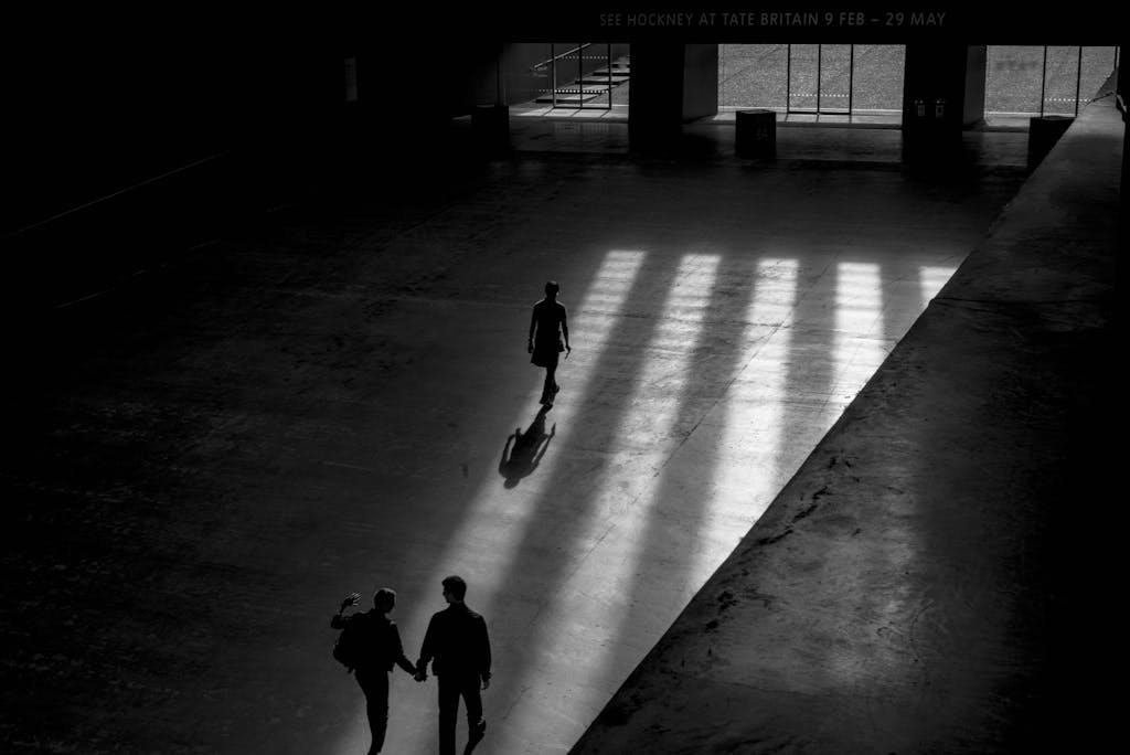 Silhouette of people walking under sunlight inside a large building.