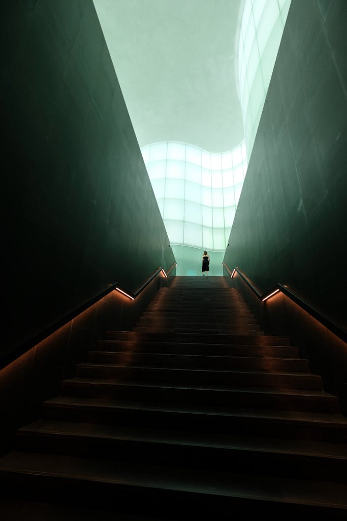 A person stands at the top of a dramatic, well-lit staircase in a modern architectural interior.