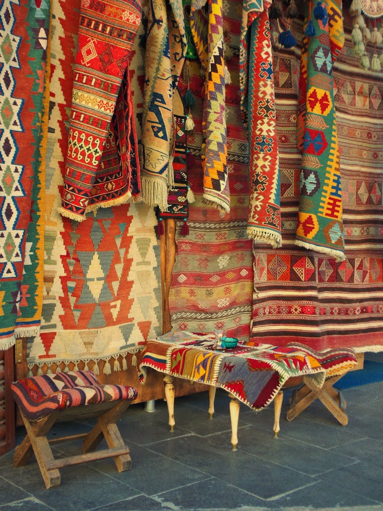 Vibrant handmade rugs with geometric patterns hung in a traditional market setting.