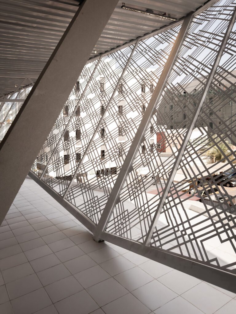 Interior architectural view looking through an intricate geometric brise-soleil screen at the Indonesian Consulate in Jeddah, displaying filtered daylight projecting patterns across raw concrete structural frames.