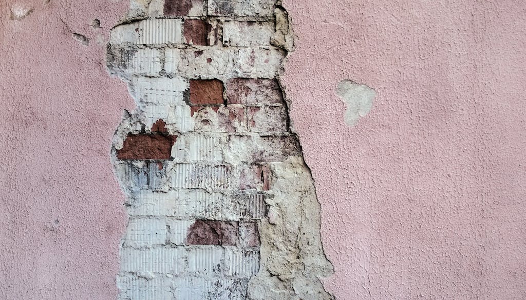 Close-up of an old brick wall with peeling plaster in soft pink tones.