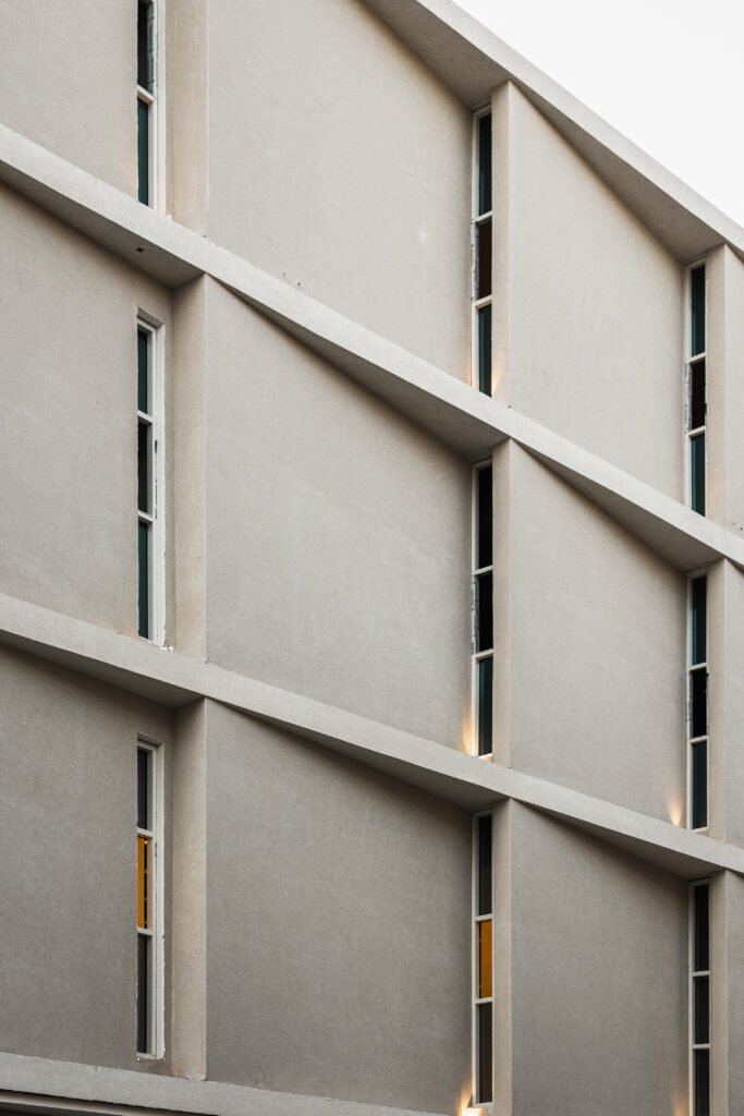Close-up exterior view of the rear facade of the Indonesian Consulate in Jeddah, showing textured concrete surfaces, continuous horizontal shading fins, and recessed vertical slot windows.