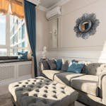 Soft couch with cushions near pouf placed at wall with mirror near big window in modern living room with bright sunlight