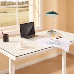 A bright modern home office with an adjustable desk, laptop, desk lamp, and design sketches by the window.