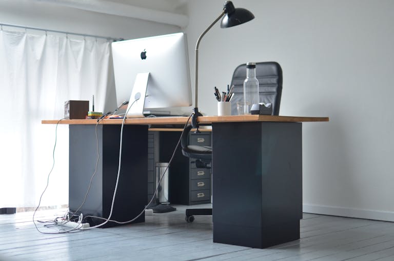 Low angle of office table with big monitor stationeries and bottle with beverage in modern workplace