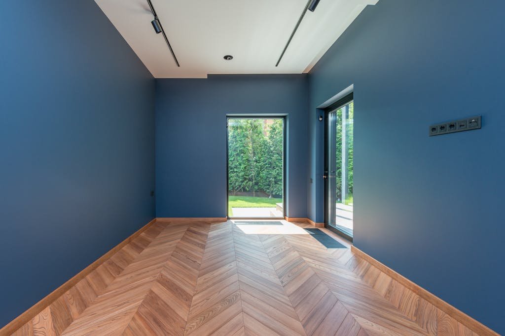 Spacious room featuring blue walls, wooden herringbone floor, and glass doors leading to a garden.