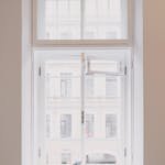 Wooden window with white frame overlooking building in city installed in light room with battery and screwdriver on windowsill in apartment