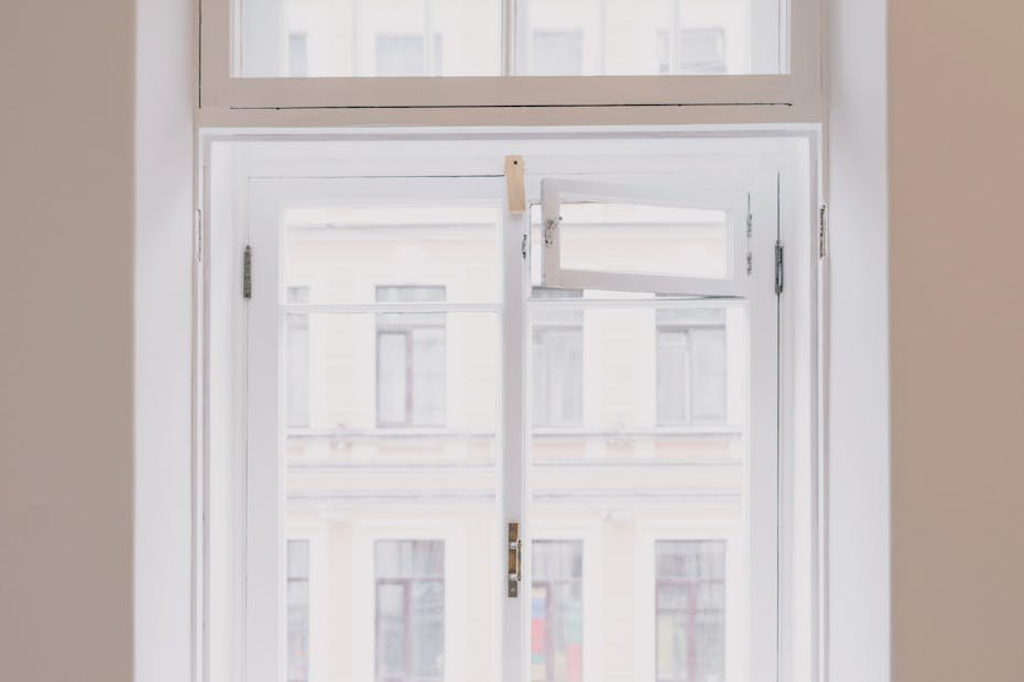 Wooden window with white frame overlooking building in city installed in light room with battery and screwdriver on windowsill in apartment