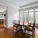 Bright dining room featuring a wooden table, classic chairs, and large windows overlooking greenery.