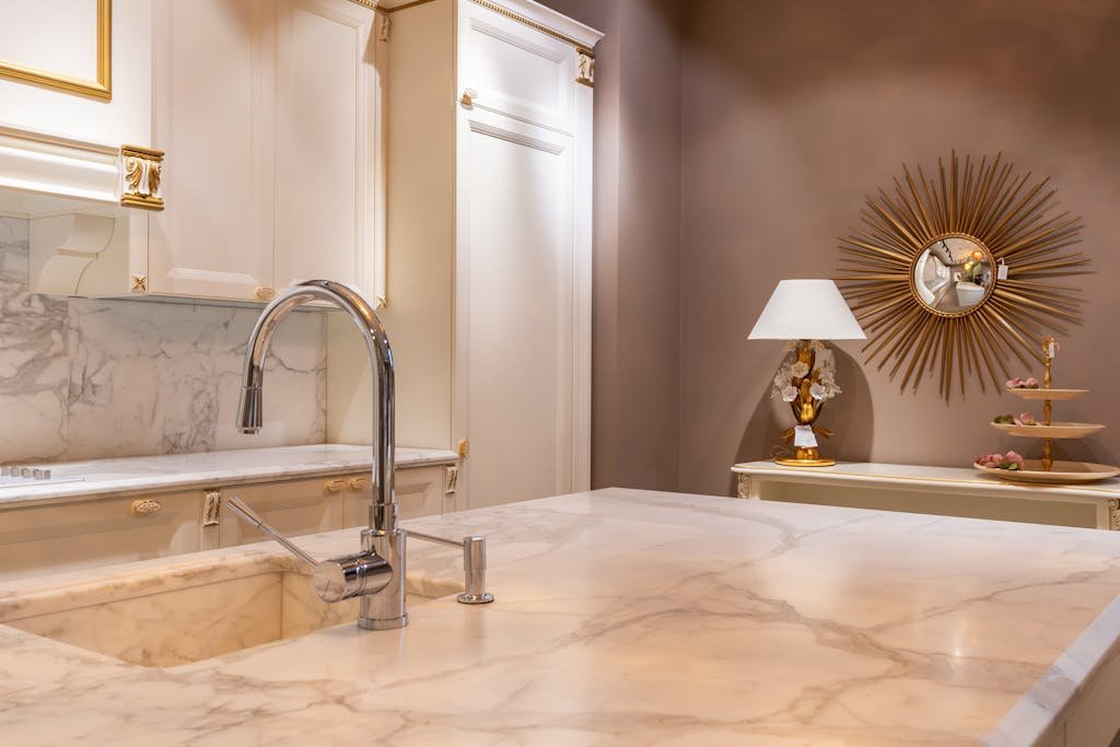Sink with faucet on marble counter in modern stylish kitchen with white cabinets and glowing lamp near decorations in apartment