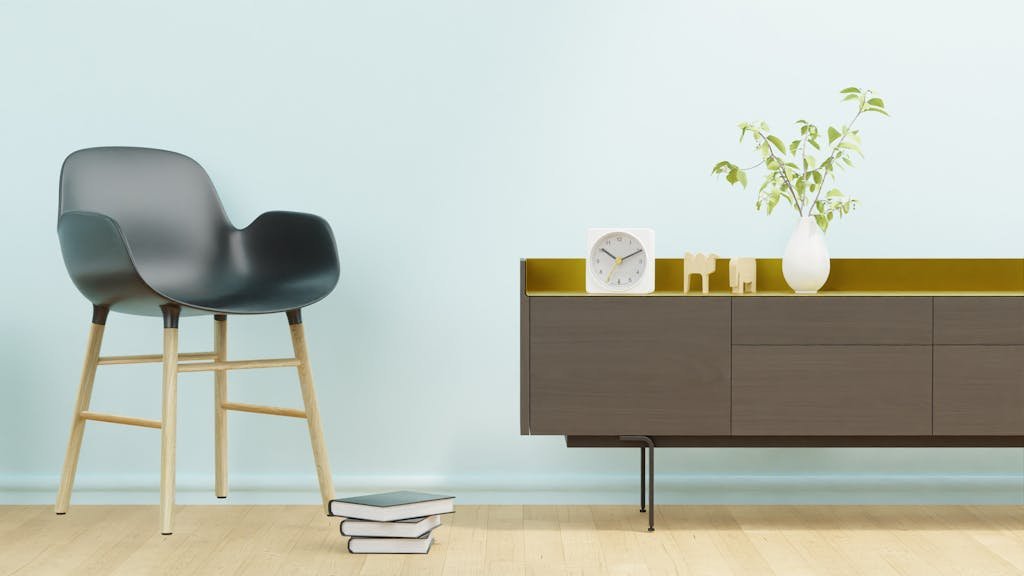 Stylish minimalist interior featuring a modern chair, stack of books, clock, and a vase on cabinet.