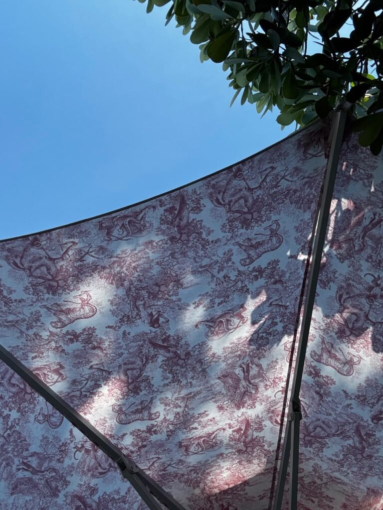Orthographic ceiling documentation of an outdoor canopy at the Dior Cafe in Miami, featuring a burgundy and off-white Toile de Jouy patterned fabric supported by a dark metal frame under a clear blue sky and green foliage.