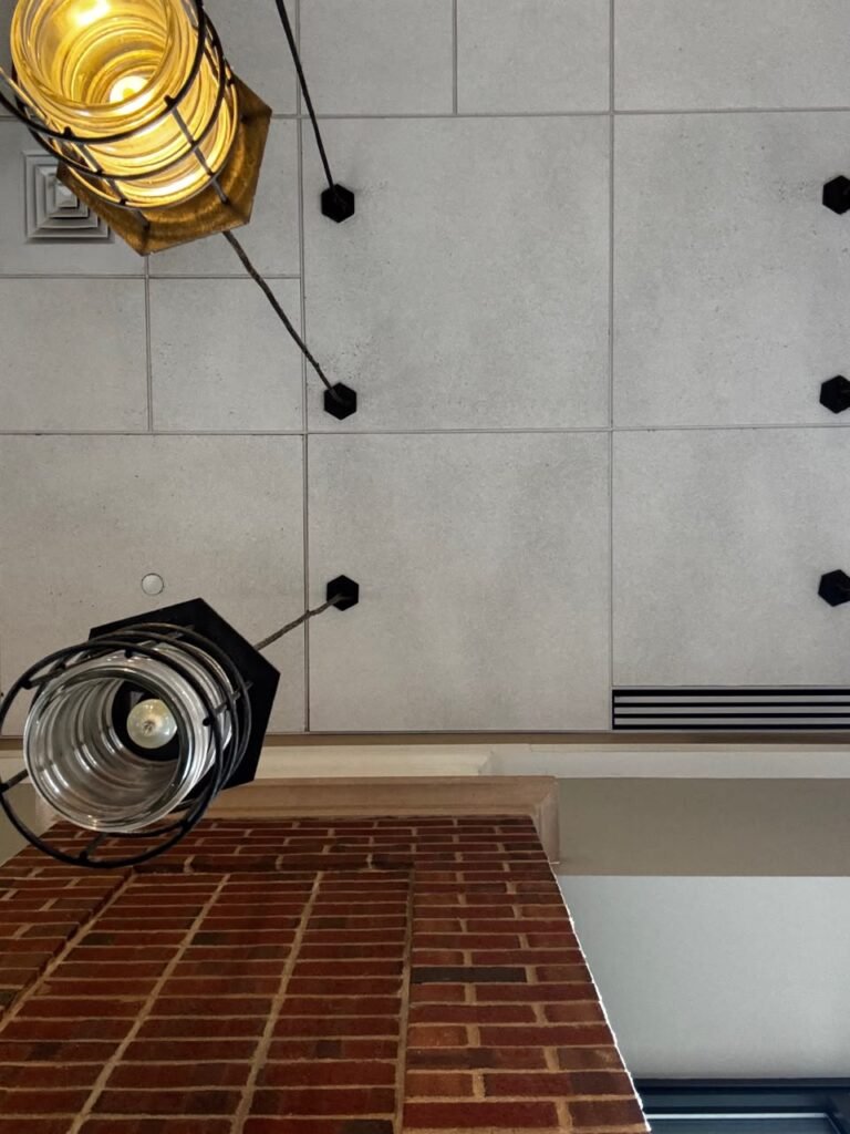 Orthographic ceiling documentation of the Hyatt Regency in New York, featuring textured grey square acoustic tiles, industrial wire-cage pendant lights, a red brick structural column, and a linear HVAC slot diffuser.