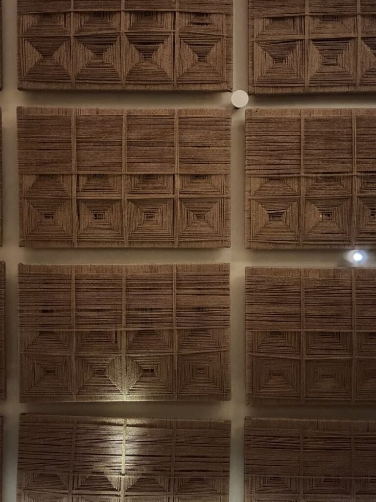 Orthographic ceiling documentation of a contemporary Saudi-style restaurant, featuring a modular grid of custom panels woven from natural brown jute rope in intricate concentric square patterns against an off-white soffit with integrated pinspots.