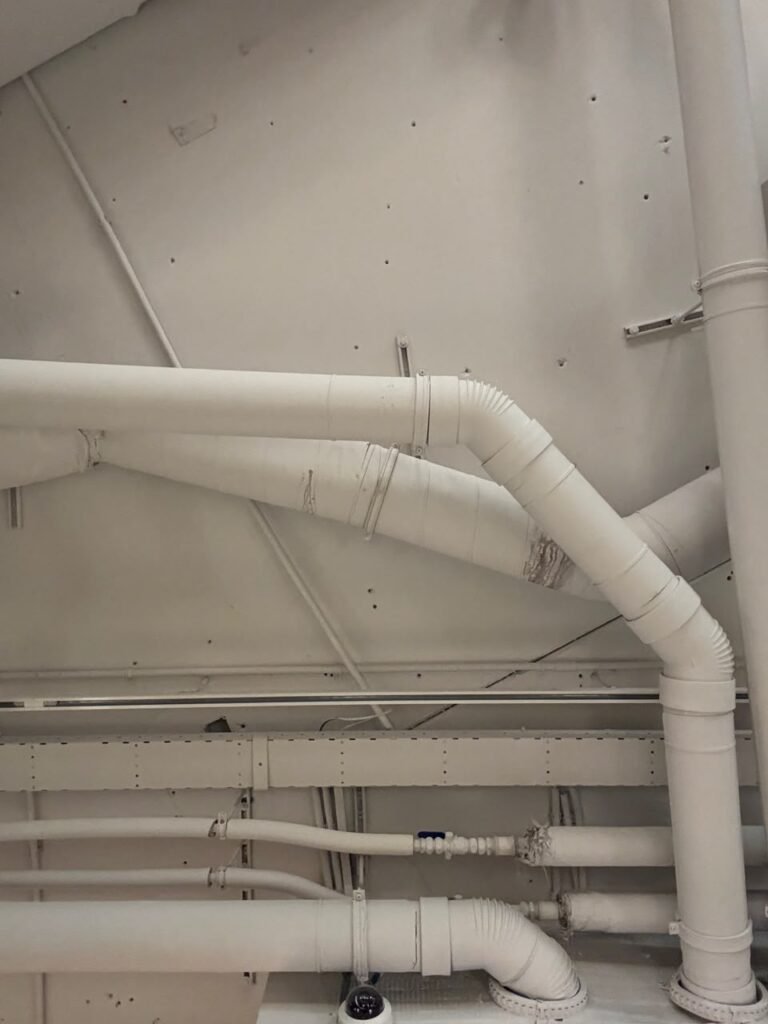 Orthographic ceiling documentation of an office space in Amsterdam, featuring an exposed open plenum with a complex network of piping, HVAC conduits, and a perforated cable tray, all uniformly finished in a matte white paint.