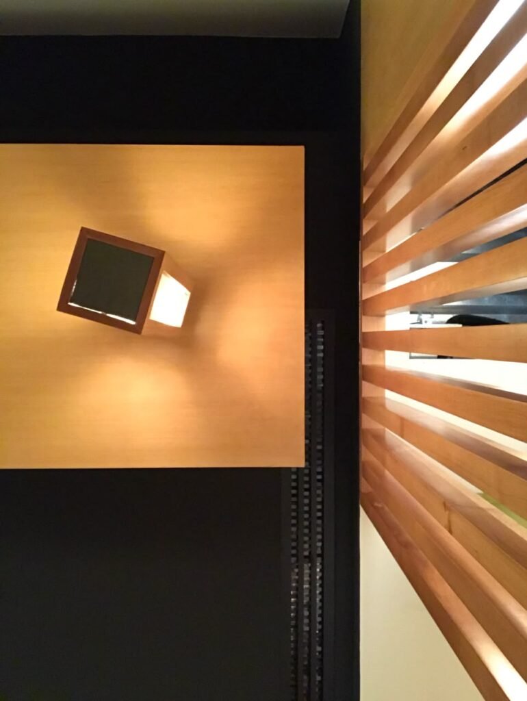 Orthographic ceiling documentation of a Japanese style interior featuring suspended beech wood panels, an angular rotated box luminaire, linear timber slats, and mechanical grilles against a black field.