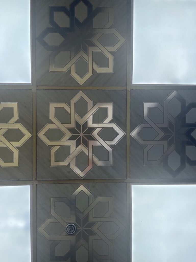 Orthographic ceiling documentation of a classic coffee shop in Jeddah, featuring a cross-shaped arrangement of grey tiled panels inlaid with metallic Islamic eight-pointed star motifs, flanked by high-luminance backlit translucent light panels.