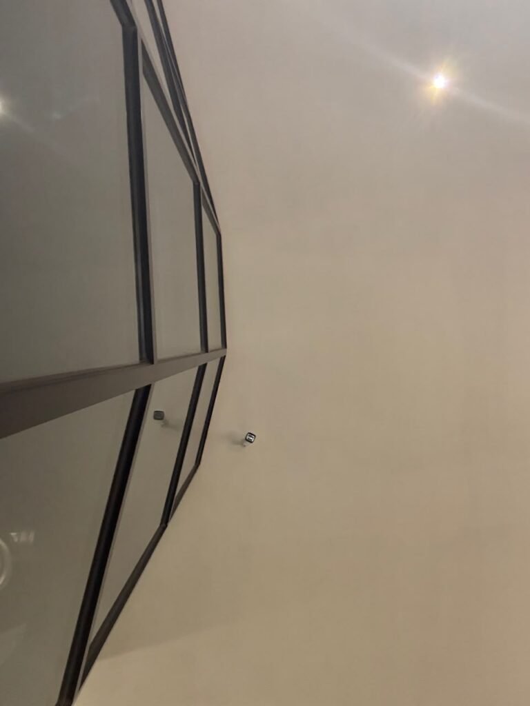 Orthographic ceiling documentation in Jeddah, capturing the sharp architectural transition between a structural dark-framed glass facade and an expansive, smooth off-white exterior gypsum soffit.