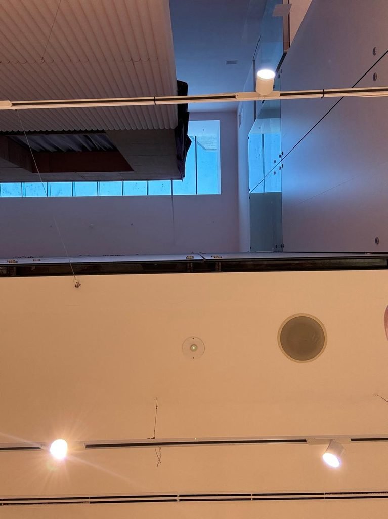 Contemporary retail store ceiling on Oxford Street London featuring a multi-story atrium void with high clerestory windows, recessed lighting tracks, white directional spotlights, and integrated ceiling utility fixtures.