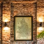A stylish living room featuring a leather sofa, brick wall, and vintage map art, enhanced by warm lighting.