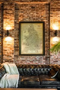 A stylish living room featuring a leather sofa, brick wall, and vintage map art, enhanced by warm lighting.