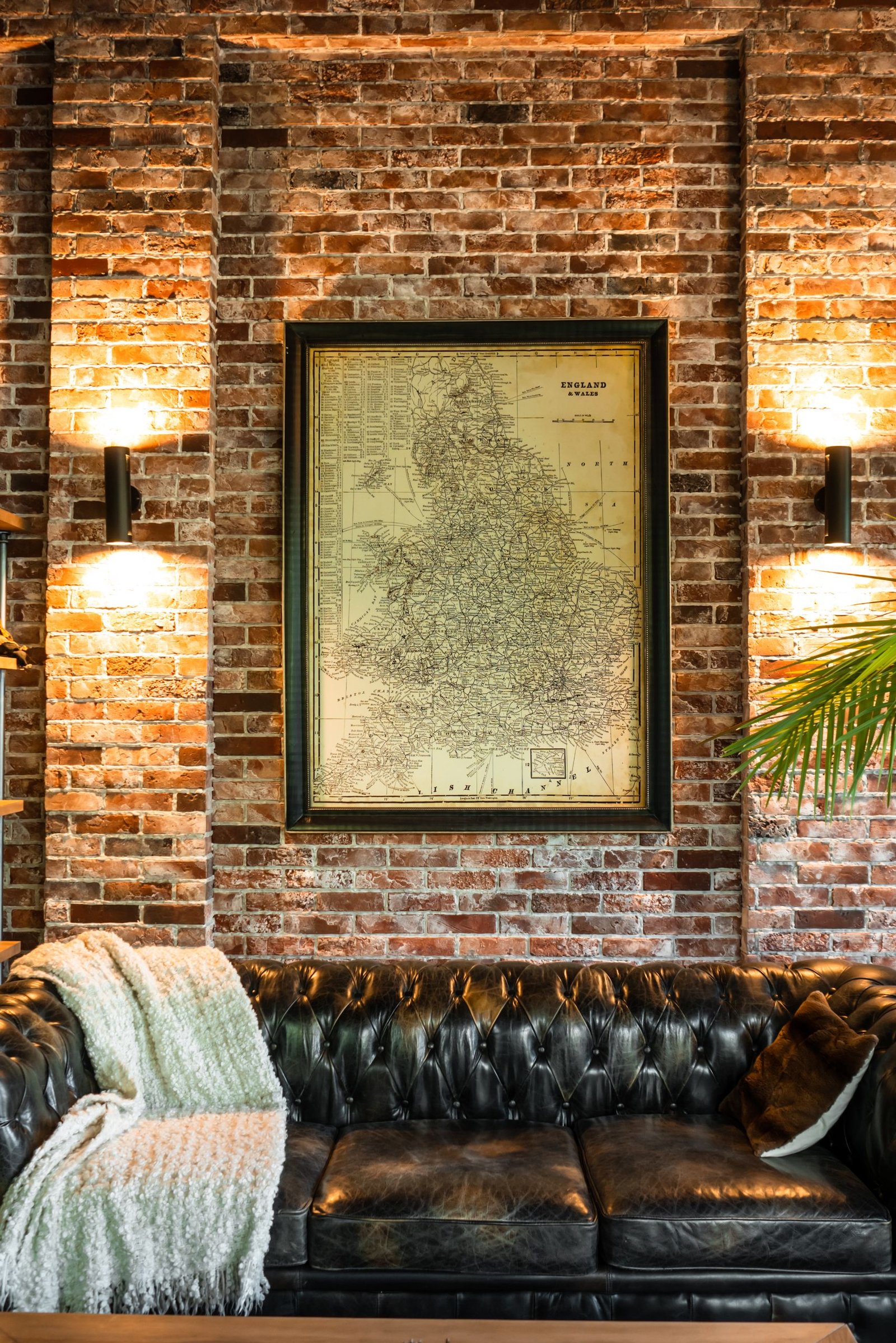 A stylish living room featuring a leather sofa, brick wall, and vintage map art, enhanced by warm lighting.