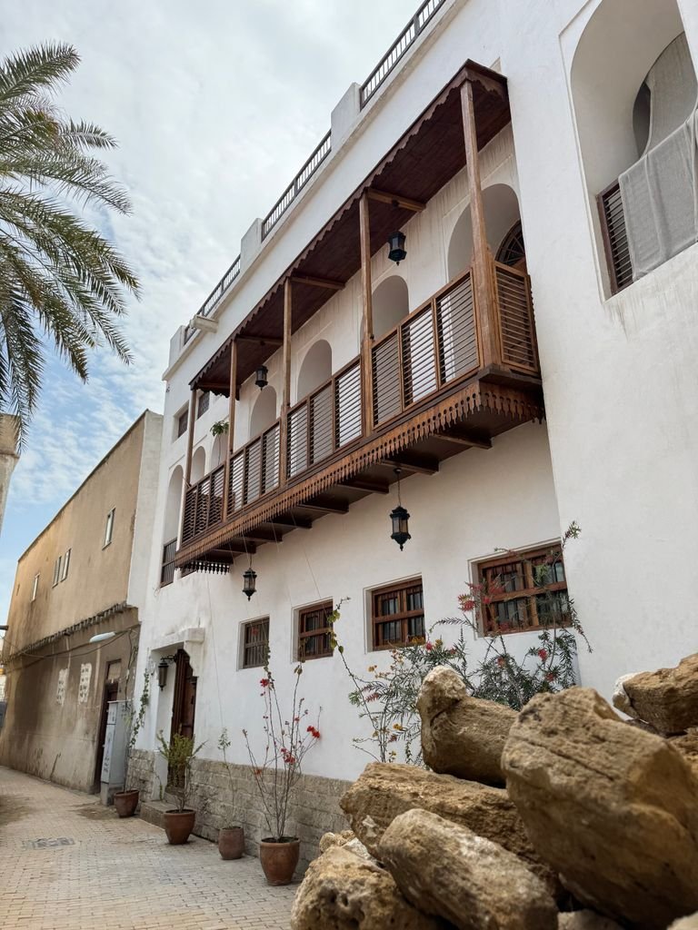 Charming Middle Eastern building with wooden balcony and palm tree accents in a sunny, serene street.
