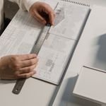 Hands of a person drafting architectural designs with a ruler on paper, indoors.